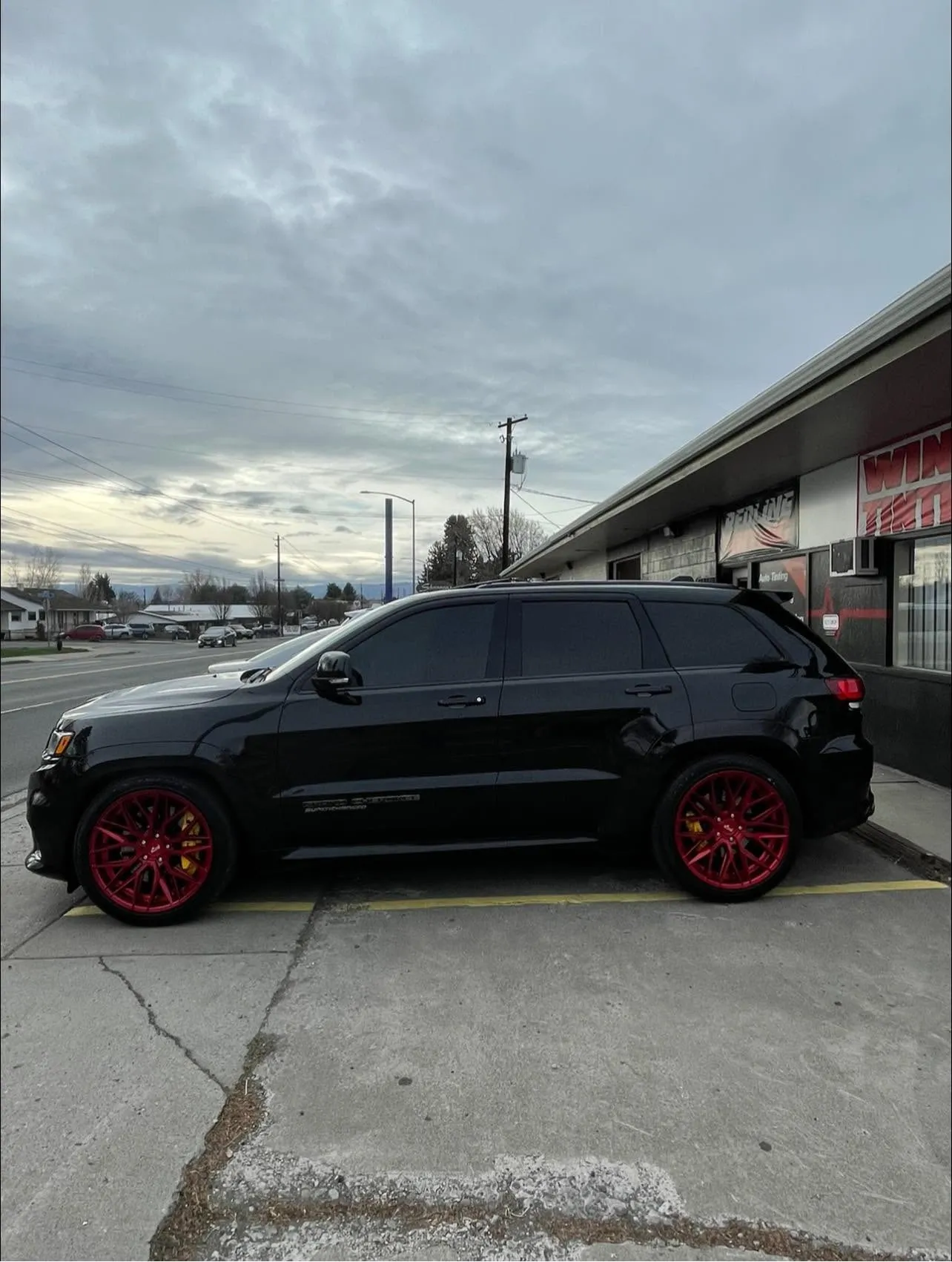 Blacked-out Jeep Grand Cherokee SRT with red wheels and dark ceramic window tint outside the Redline Tinting shop at dusk