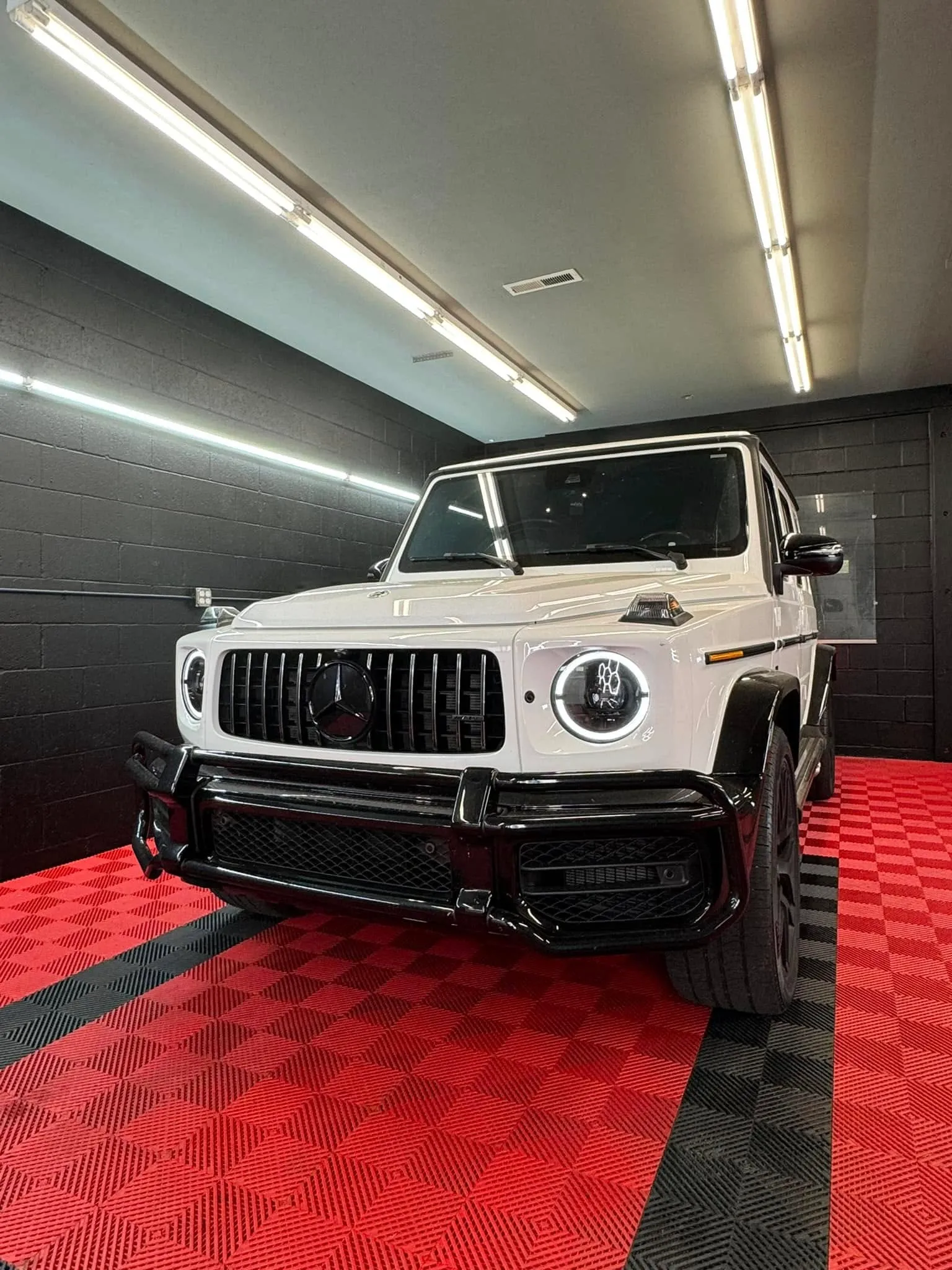 White Mercedes-Benz G63 AMG front view inside the Redline Tinting shop with LED bay lighting and the shop's red diamond floor