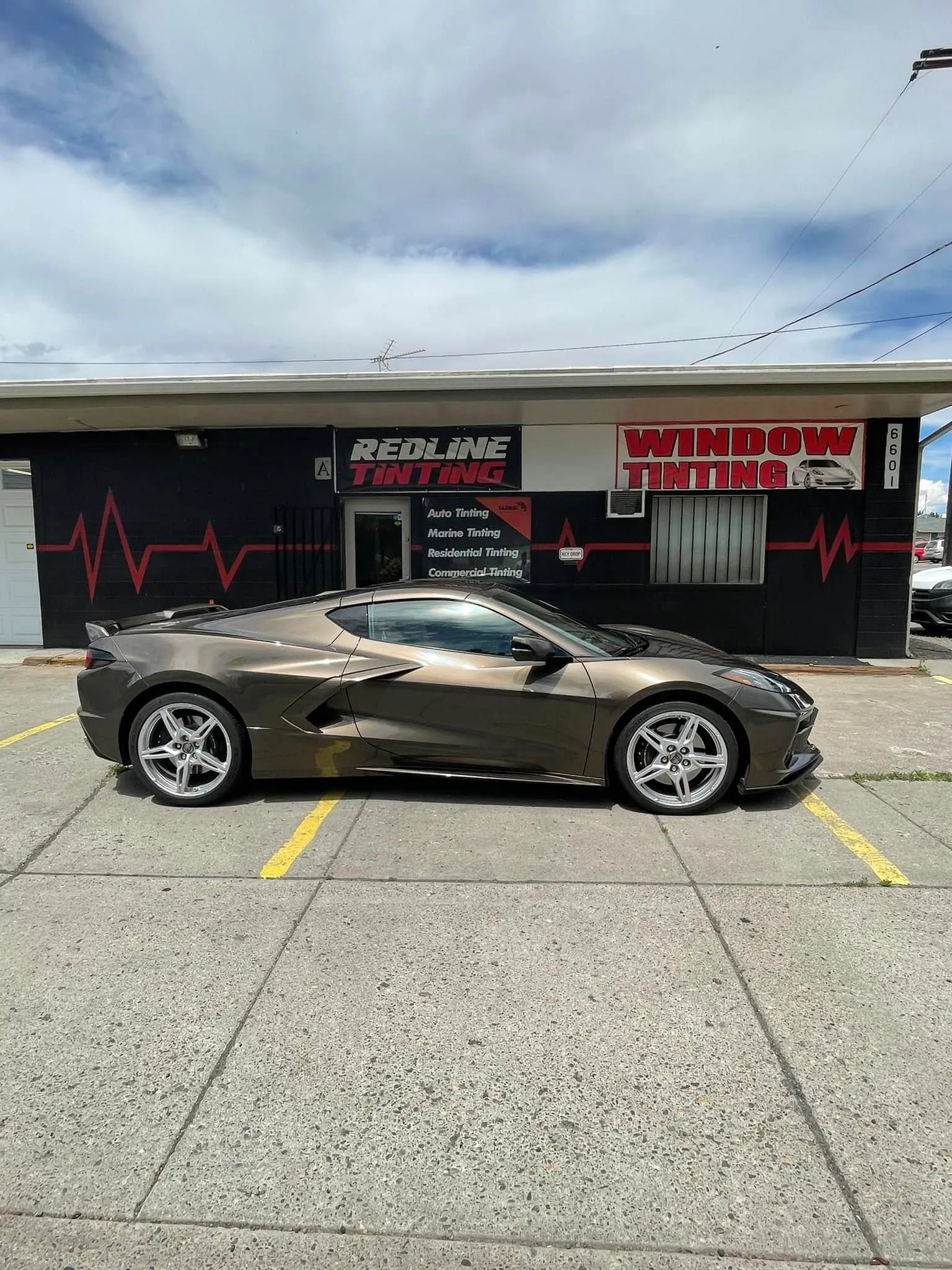 Bronze Chevrolet Corvette C8 with fresh window tint parked in front of the Redline Tinting storefront in Yakima with the red heartbeat EKG signage visible